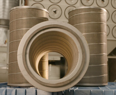 Replacement dust collector cartridge filters in a set of three with a dust collection system in the background.