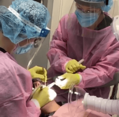 Dental professionals working on a patient while the fume extractor hood captures VOCs and other airborne contaminants.