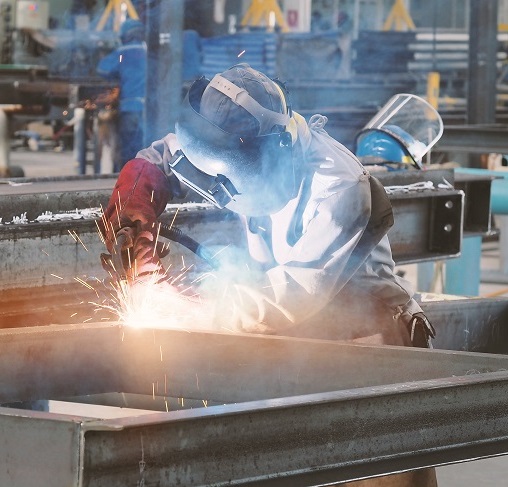 A machine operator working on a welding project. Fumes and sparks are shown transmitting into the surrounding air.